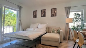 Ein Schlafzimmer mit Bett, einer Couch, einer Lampe und Blick auf Bäume durch das Fenster.