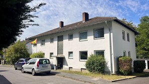 A two-story building with a flat roof, multiple windows, and a flag on the left side.