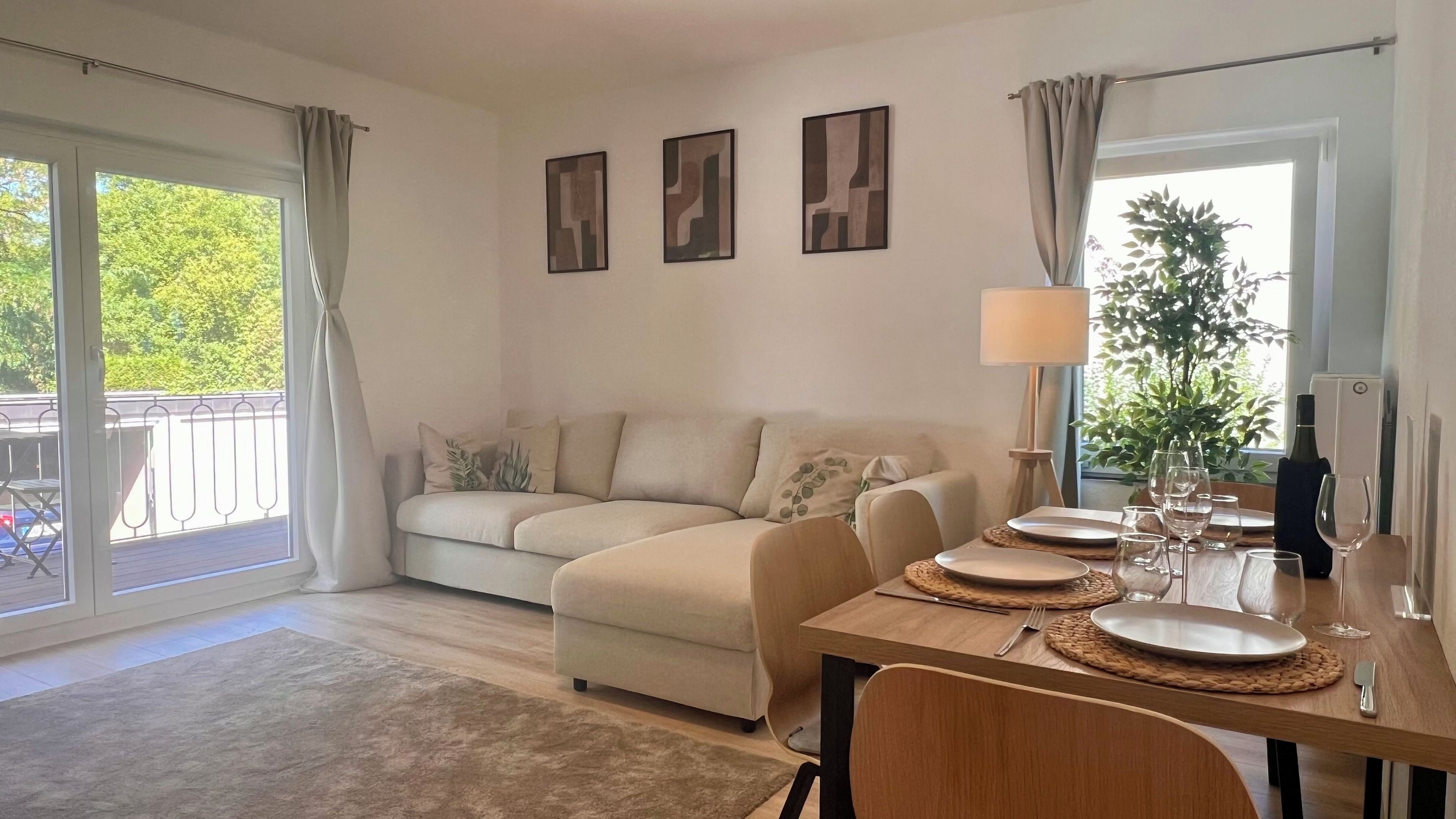 Ein Wohnzimmer mit Sofa, Esstisch für vier Personen und einem Balkon mit Blick auf Grünflächen.
