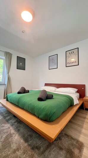 Ein Schlafzimmer mit einem Bett, einem Kopfteil, einem Fenster mit Vorhängen und Wandbildern.