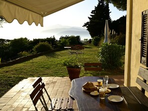 An outdoor dining area with a table set for two, a bench, and a view of a mountainous landscape. - Innamorata Casa Elisio (Capoliveri)