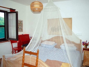 A bedroom with a bed covered by a mosquito net, a red dresser, a wooden chair, and a hanging light fixture. - Innamorata Casa Elisio (Capoliveri)