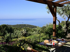 A picnic table with food and drinks, overlooking a coastal landscape with hills and a clear sky. - Innamorata Casa Elisio (Capoliveri)