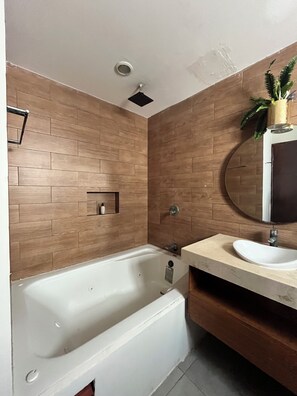 Un baño moderno con una bañera independiente, un espejo redondo y un diseño de pared de madera.
