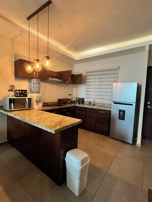 Una cocina moderna con una isla central, electrodomésticos de acero inoxidable e iluminación colgante.
