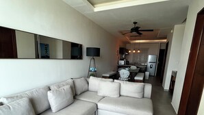 A modern living room with a sectional sofa, a dining area, and a kitchen in the background. - Private apartment | Pool and beach views | Sleeps 7 | Fully equipped | Wi-Fi and balcony (Mahahual)