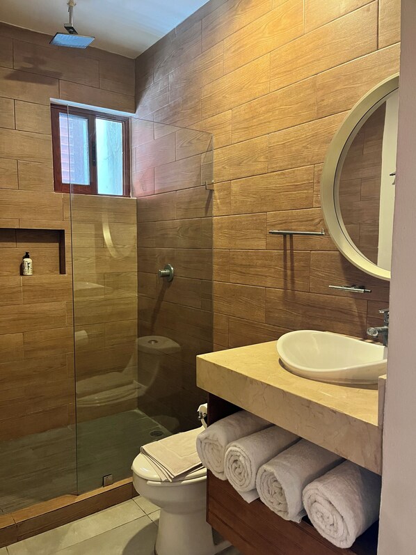 Un baño moderno con ducha envuelta en vidrio, inodoro, lavabo con espejo y toallas dobladas con cuidado.