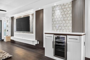 A modern living room with a flat-screen TV, built-in entertainment unit, and a wine cooler. - The Baycrest | Heated Pool, Beach and Bay Access (Treasure Island)