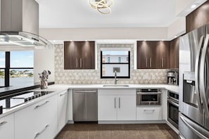 A modern kitchen with stainless steel appliances, white cabinetry, and a view of the city. - The Baycrest | Heated Pool, Beach and Bay Access (Treasure Island)