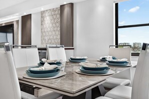 A modern dining area with a large table, white chairs, and blue plates. - The Baycrest | Heated Pool, Beach and Bay Access (Treasure Island)