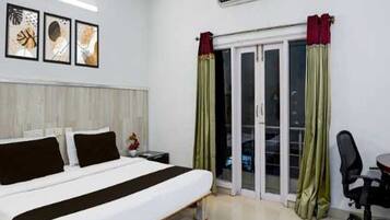 A hotel room with a bed, a desk, and a chair. There is a window with curtains, and a ceiling fan is visible.