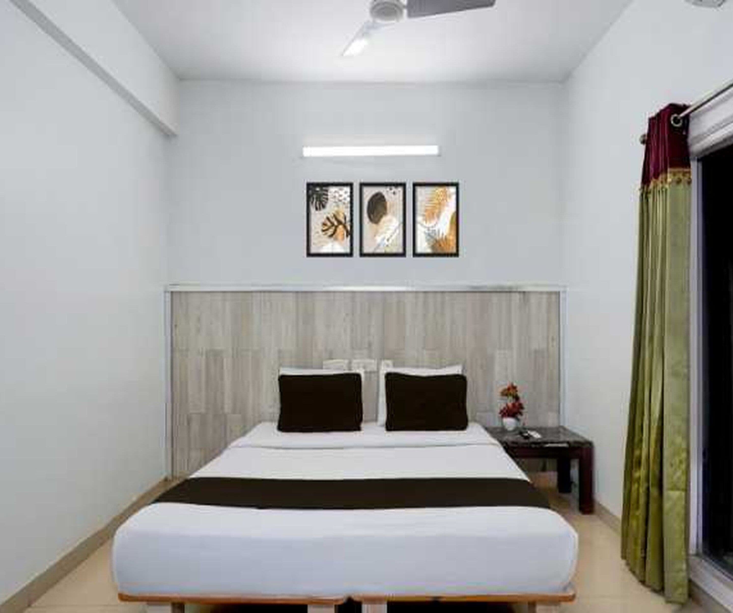 A bedroom with a bed, a nightstand, a window with curtains, and three wall-mounted pictures.