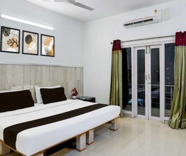 A hotel room with a bed, a nightstand, a wall-mounted air conditioner, and a sliding glass door leading to an outdoor area.