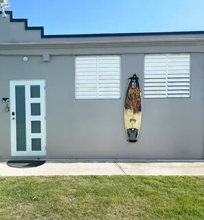 A building with a grey exterior, a white door, and a surfboard mounted on the wall. - Cozy Aguada, PR Studio, Relax, Unwind & Enjoy (Aguada)