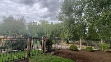 Un jardin clos, délimité par une clôture et doté d’un portail, entouré d’arbres et d’arbustes.