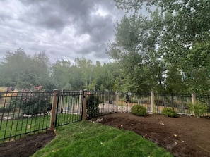 Un área de jardín cercada con una puerta, rodeada de árboles y arbustos.