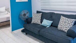 Habitació amb una paret d'accent blau, un sofà gris amb coixins estampats, un ventilador i un llit amb roba de llit blanca.