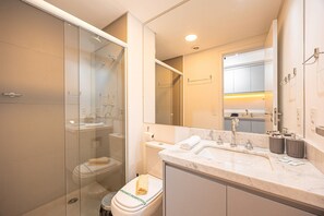 Ein modernes Badezimmer mit einer gläsernen Duschkabine, einer Toilette mit Papierhandtuchhalter und einem Waschbecken mit Marmorplatte.