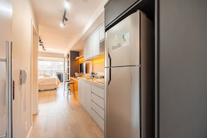 Eine moderne Küche mit integriertem Kühlschrank, eine Essecke mit Barhocker und ein Schlafzimmer mit Bett und Fenster.