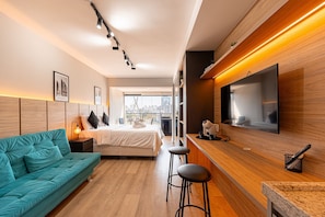 Ein modernes Hotelzimmer mit einer Couch, einem Bett, einem Fernseher und einem Balkon mit Blick auf die Stadt.
