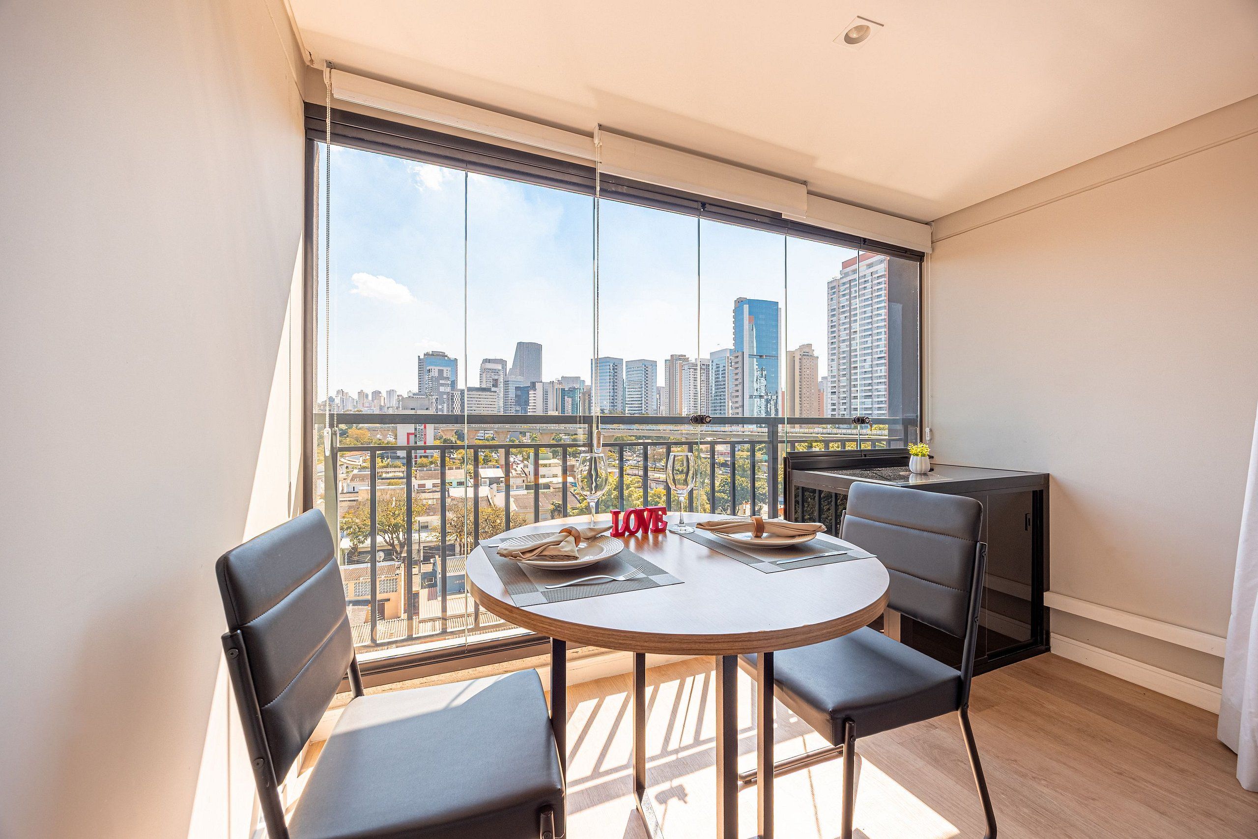 A balcony with a table set for two, overlooking a cityscape.