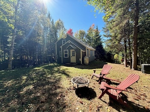A cabin with a fire pit and Adirondack chairs in a forested area.