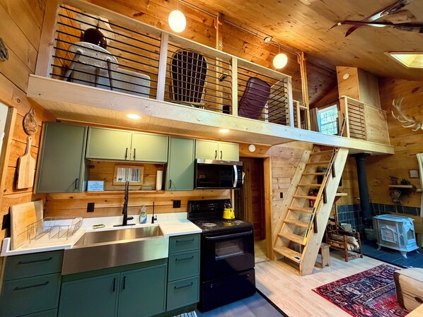 A wooden interior with a kitchen, a dining area, and a loft space with a ladder.