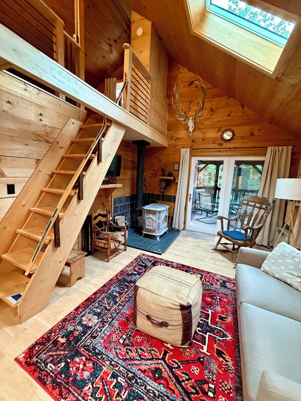 A wooden interior with a staircase, a fireplace, a sofa, and a rug.