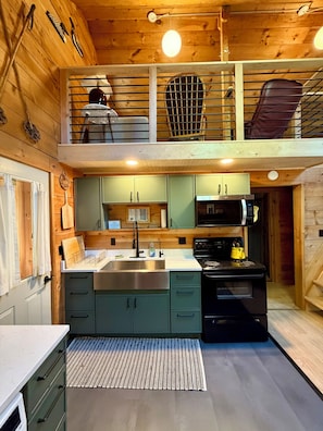 A modern kitchen with a two-tiered design, featuring a stainless steel sink, a black stove, and green cabinets.