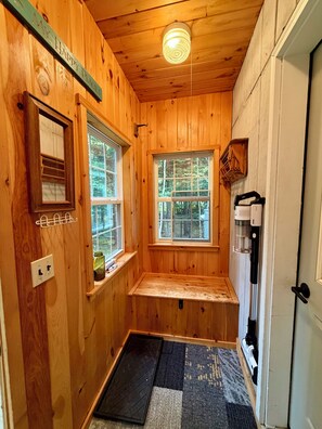A small, wooden cabin with two windows, a bench, a coffee maker, and a door.