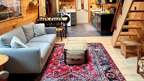 A cozy cabin interior with a sofa, ottoman, and a patterned rug. - Lazy Pine Lodge - just 10 minutes from Sugarloaf! (Stratton)