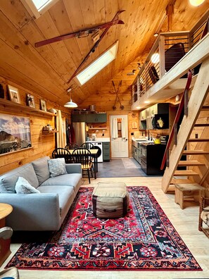 A cozy cabin interior with a sofa, ottoman, and a patterned rug.
