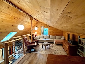 A cozy wooden cabin with a loft bedroom, a sofa, a chair, and a small table.