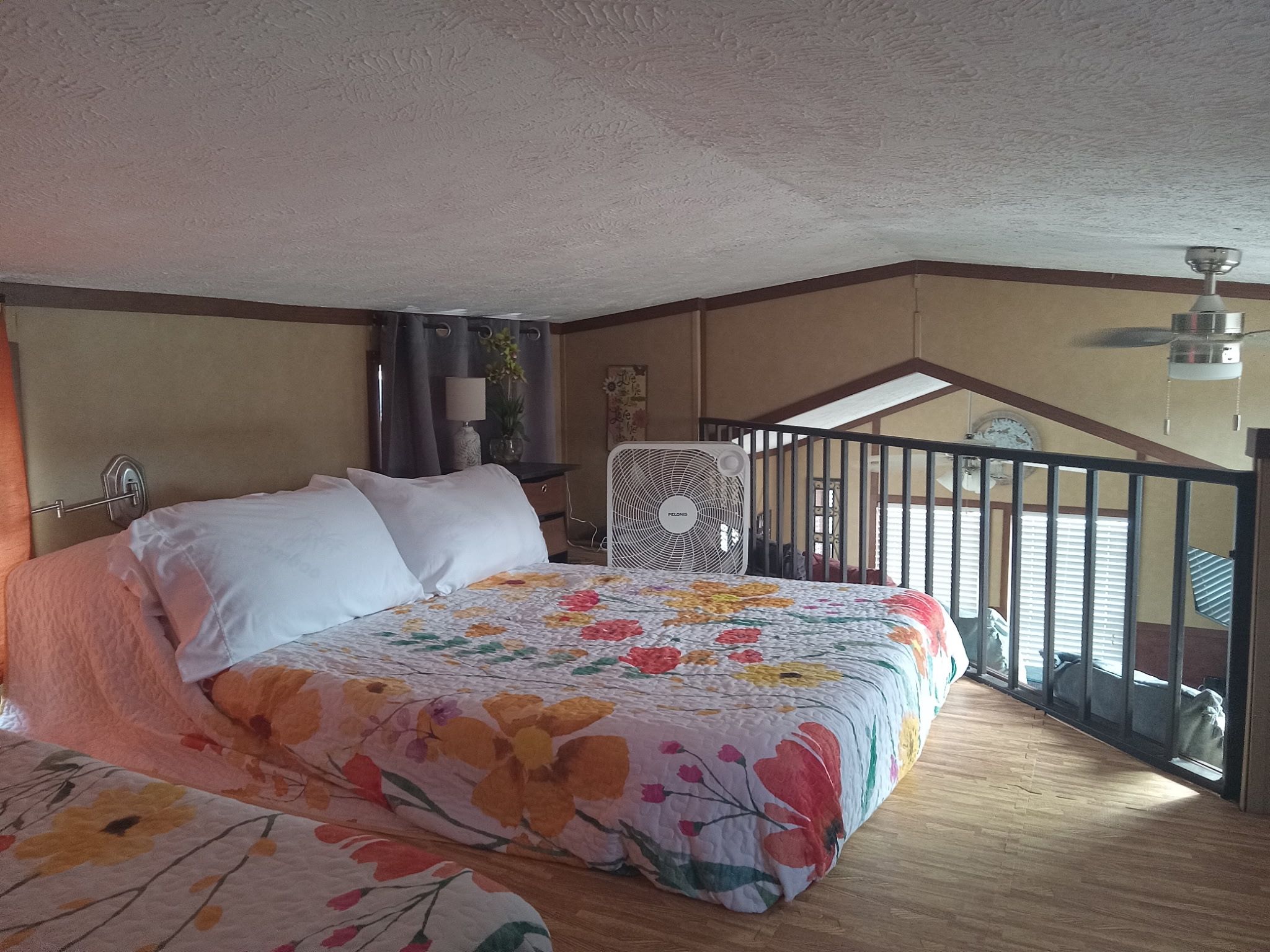 Une chambre dotée d’un grand lit, d’un ventilateur de plafond, d’une fenêtre avec des stores et offrant une vue sur l’extérieur.
