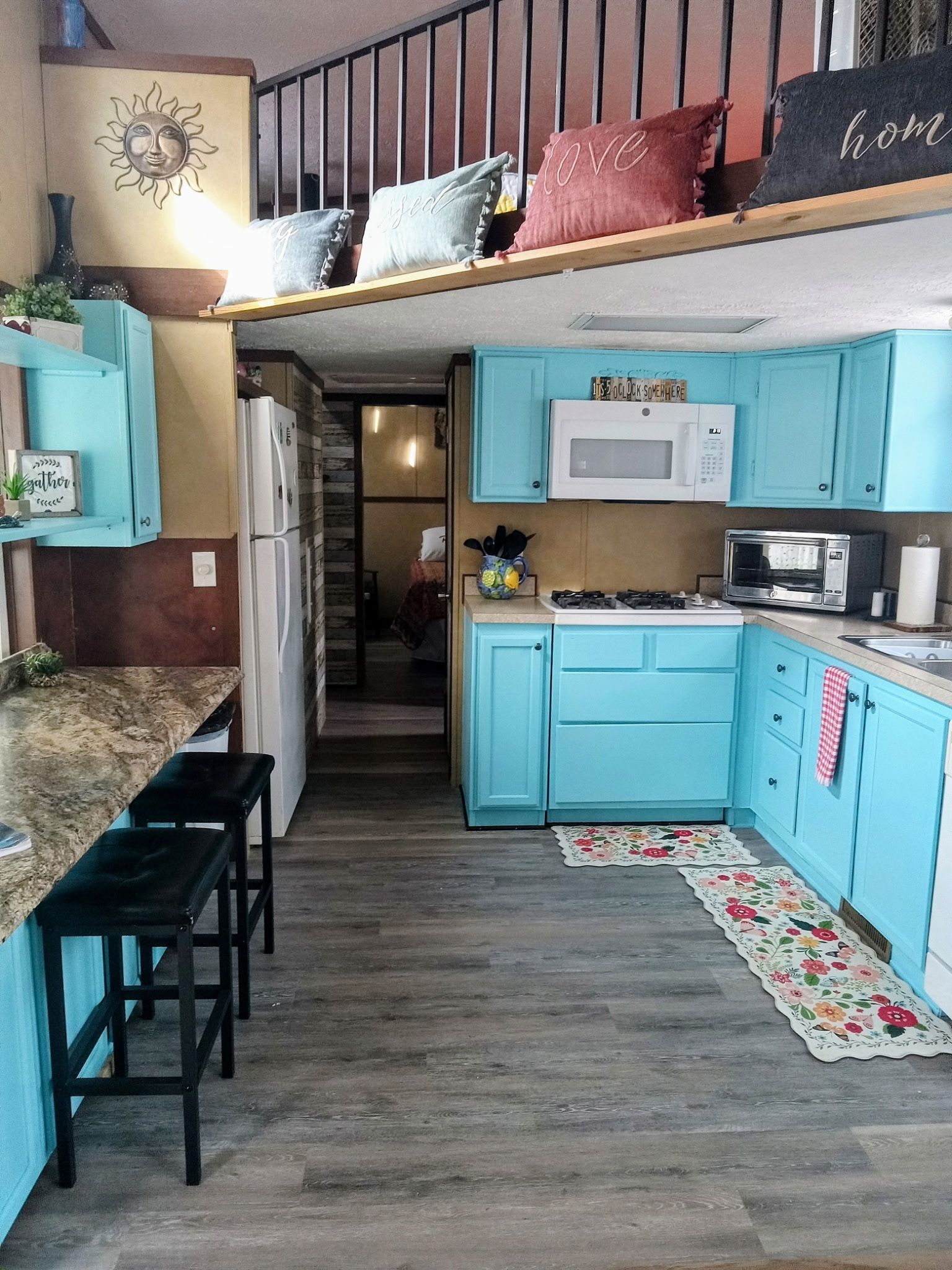 A compact kitchen with teal cabinets, a microwave, and a gas stove. There is a wooden bench and a small island with a sink.