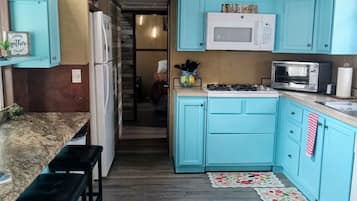 A compact kitchen with teal cabinets, a microwave, and a gas stove. There is a wooden bench and a small island with a sink.