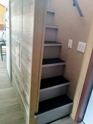 A staircase with a wooden handrail and a beige wall. - The Cabana (Conway)