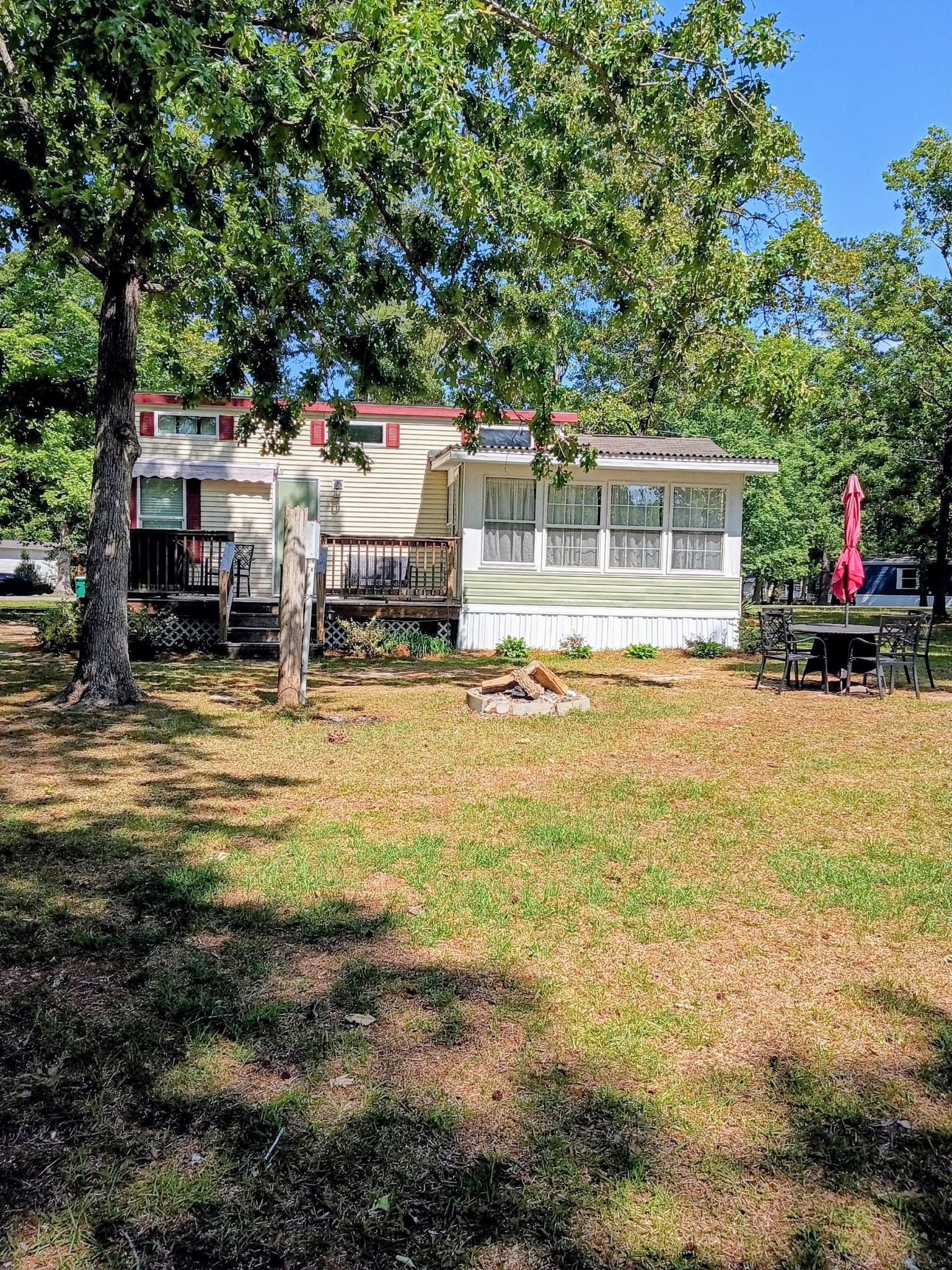 A mobile home with a fenced yard, a picnic table, and a red umbrella.
