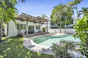 Ein modernes Haus mit Pool, einer Pergola und einer Terrasse mit Gartenmöbeln.