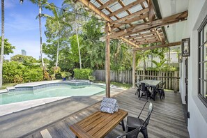 Ein Garten mit Holzterrasse, Pool und einer Pergola mit Lichterketten.