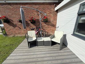 Un patio al aire libre con mobiliario de mimbre, una bicicleta y macetas con flores frente a un muro de ladrillo.