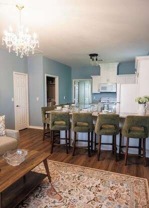 A modern kitchen with white cabinets, a central island with bar stools, and a chandelier. - Relaxing French Country House-Pool- Hot Tub- by The Strand, Beach, Pleasure Pier (Galveston)