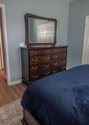A bedroom with a dark wooden dresser, a mirror, and a blue bedspread. - Relaxing French Country House-Pool- Hot Tub- by The Strand, Beach, Pleasure Pier (Galveston)