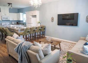 A modern kitchen with white cabinets, a dining area with a large island, and a living room with a sofa and a TV. - Relaxing French Country House-Pool- Hot Tub- by The Strand, Beach, Pleasure Pier (Galveston)