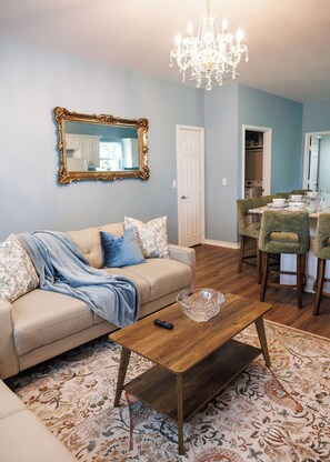 A living room with a sofa, coffee table, and a chandelier. - Relaxing French Country House-Pool- Hot Tub- by The Strand, Beach, Pleasure Pier (Galveston)
