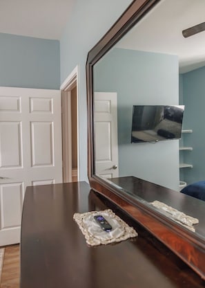 A room with a wooden dresser, a large mirror, and a television on the wall. - Relaxing French Country House-Pool- Hot Tub- by The Strand, Beach, Pleasure Pier (Galveston)