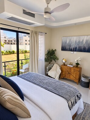 A bedroom with a bed, a ceiling fan, a view of the outside, a wooden cabinet, and a painting on the wall. - Chic 1BR Island Retreat |  Paradisiac, Jamaica (Llandovery)