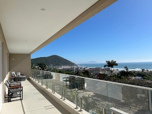 Ein Balkon mit Glasgeländer, der Blick auf eine Küstenstadt und das Meer bietet.