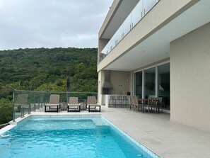 Ein Pool mit Liegestühlen und Essbereich, umgeben von einem modernen Gebäude mit großen Fenstern.