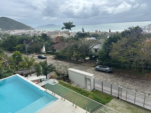 Ein Wohngebiet mit Schwimmbad, einer Straße mit parkenden Autos und Blick auf das Meer und die entfernten Hügel.